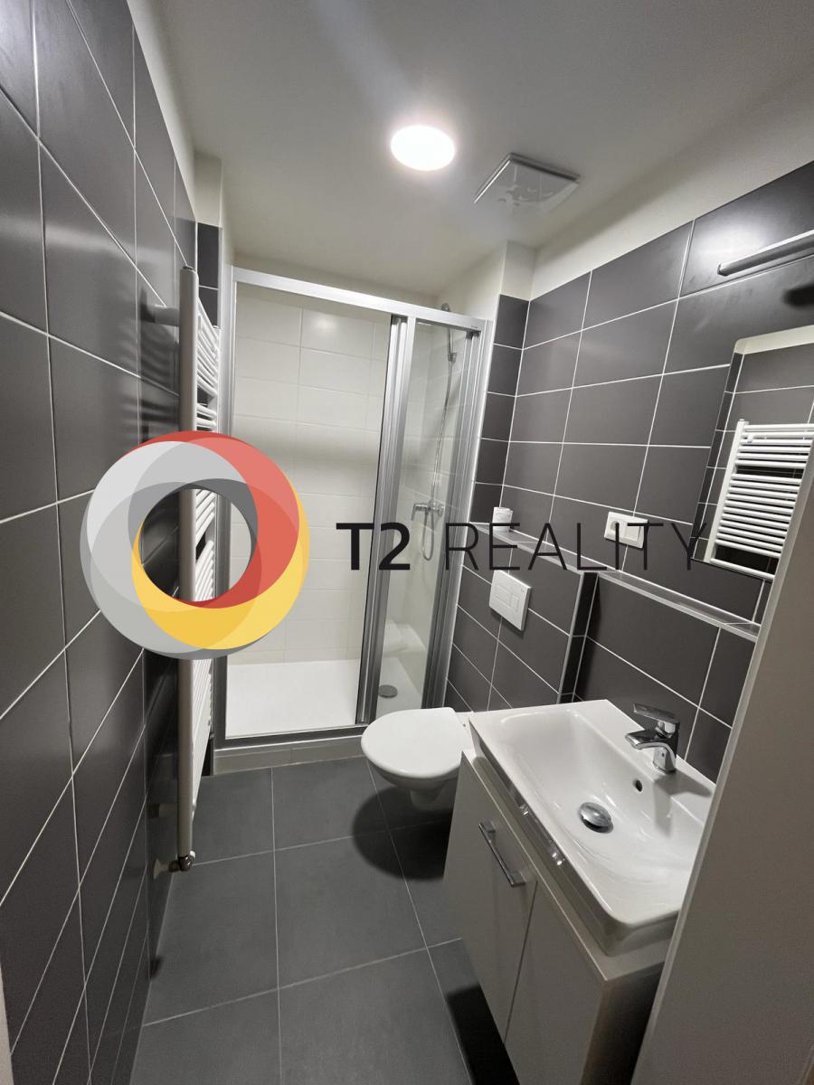 חדר אמבטיה מרוצף אפור כהה עם מקלחון, ארון כיור ומייבש מגבות