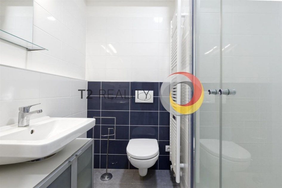 חדר אמבטיה בחיפוי לבן עם קיר כחול כהה, מקלחון זכוכית וארון כיור